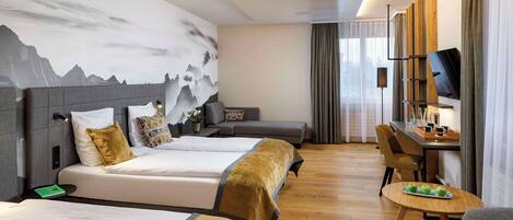 A hotel room with two beds, a desk with a TV, a dining table with apples, and a mountain mural on the wall.