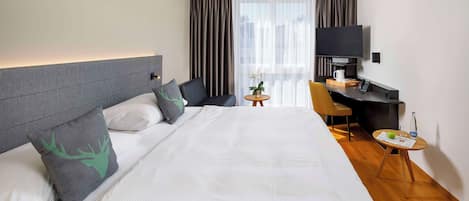 Ein Hotelzimmer mit einem großen Bett, einem Schreibtisch mit Stuhl, einem Fernseher und einem kleinen Tisch mit Pflanze und Glas.