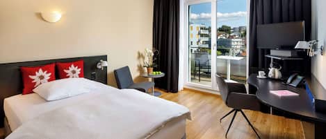 Habitación de hotel con cama, escritorio, silla, televisión y balcón con vista a la ciudad.
