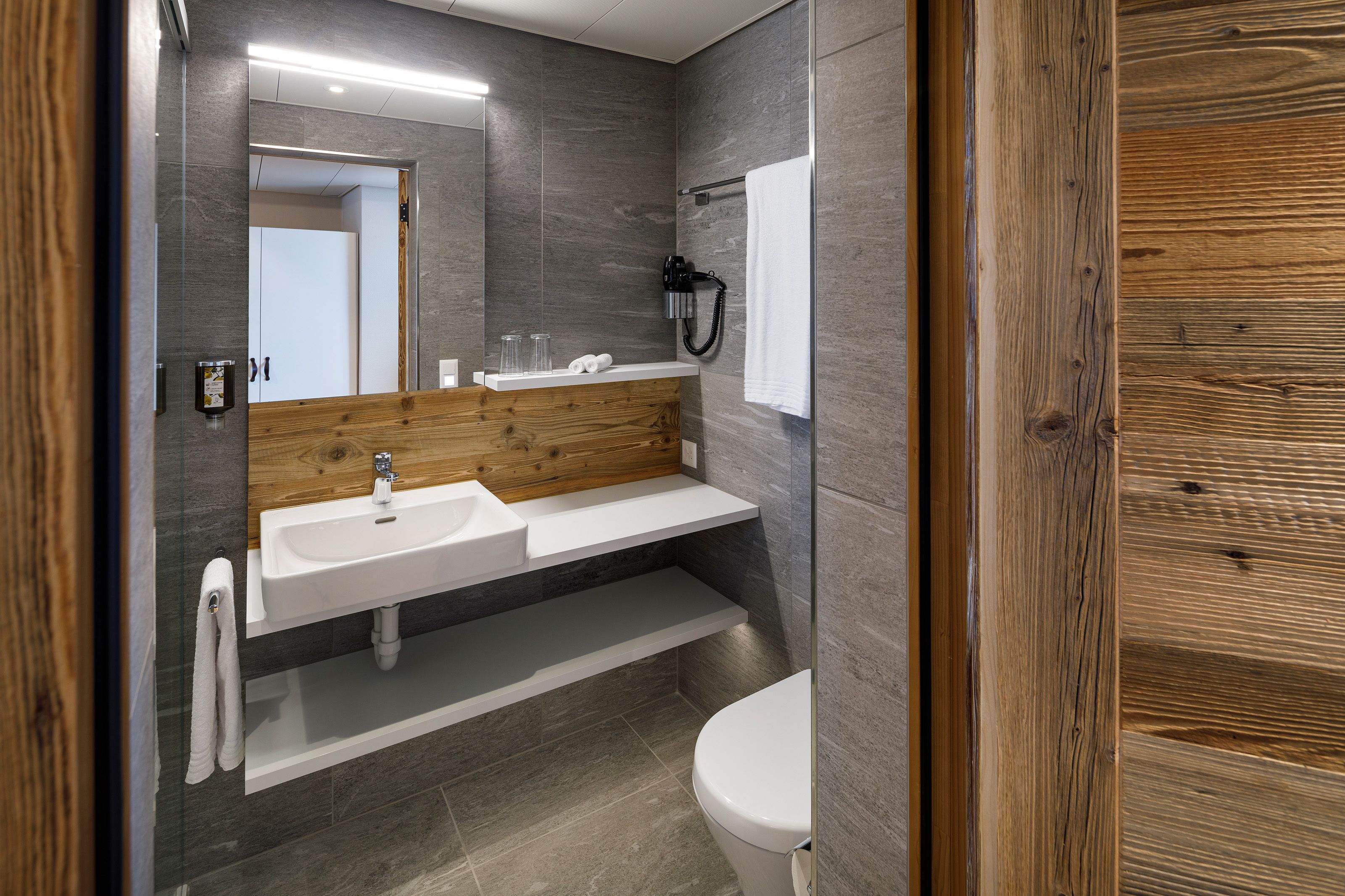 A modern bathroom with a wooden vanity, a white sink, a mirror, and a towel rack.