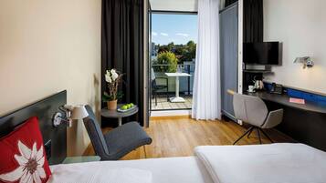 A hotel room with a bed, a desk, a chair, a TV, and a balcony with a table and chairs.