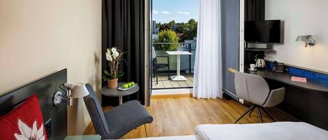 A hotel room with a bed, a desk, a chair, a TV, and a balcony with a table and chairs.