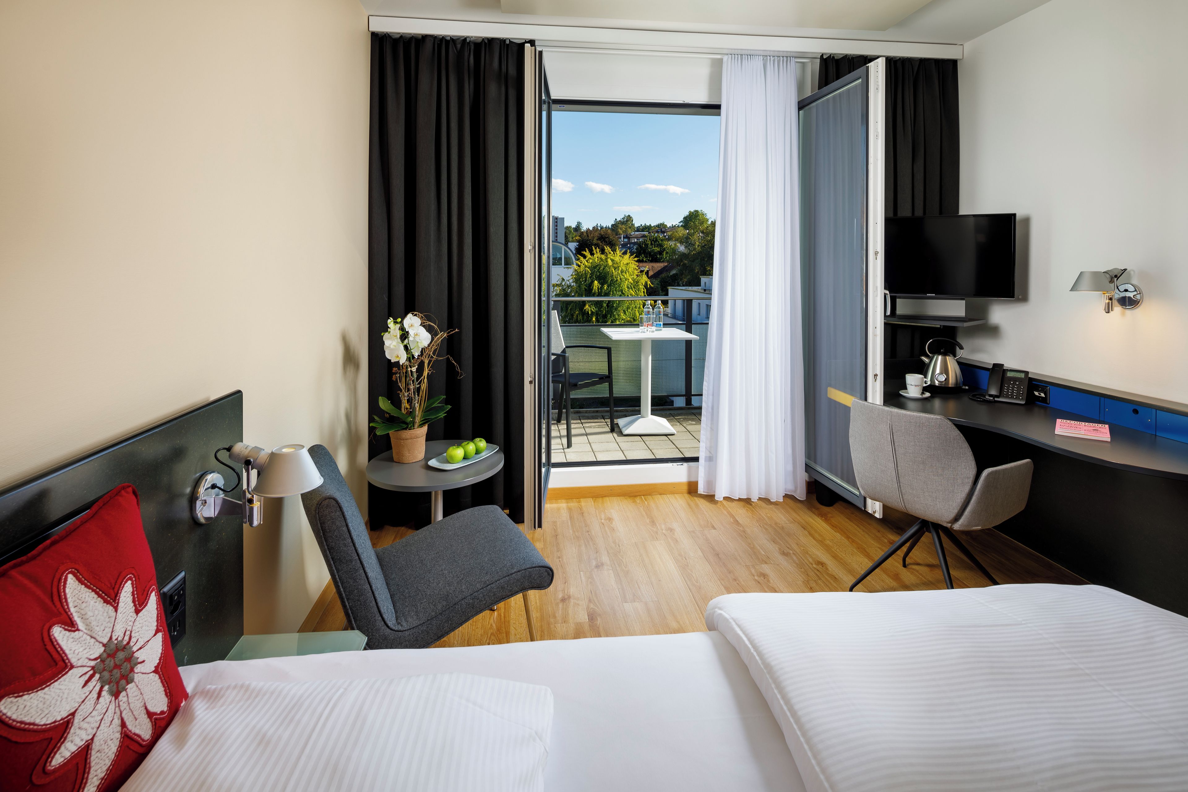 Une chambre d’hôtel comprenant un lit, un bureau avec une chaise, une télévision et un balcon avec une table et des chaises.