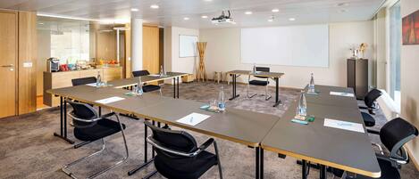 A conference room with a long table, chairs, a projector, and a whiteboard.