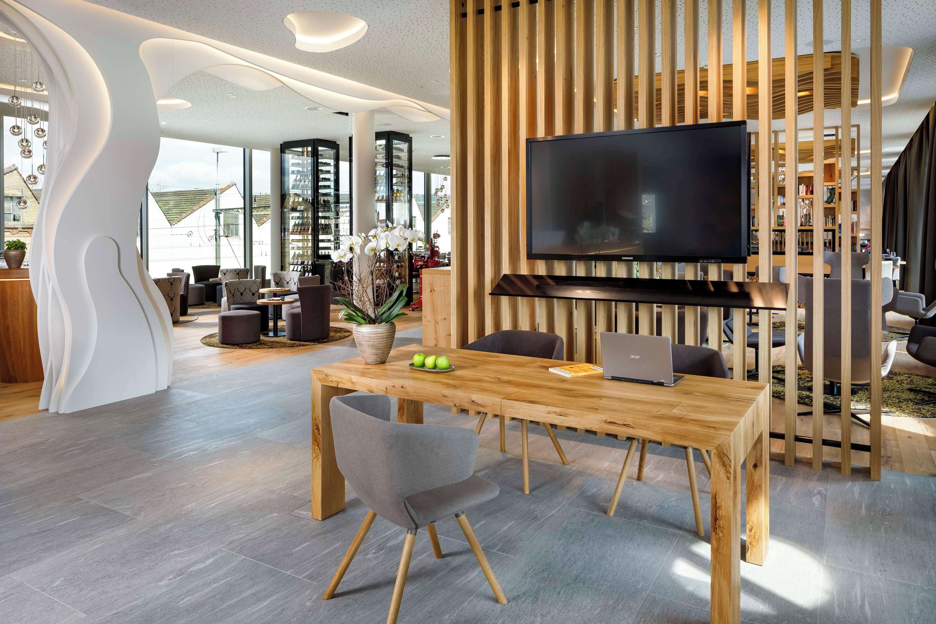 Un espace repas moderne avec une table en bois, des chaises grises, un téléviseur à écran plat et un paravent décoratif en bois.