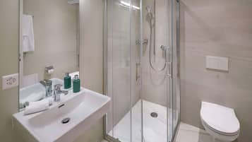 Un baño moderno con ducha de vidrio, lavamanos blanco y retrete.