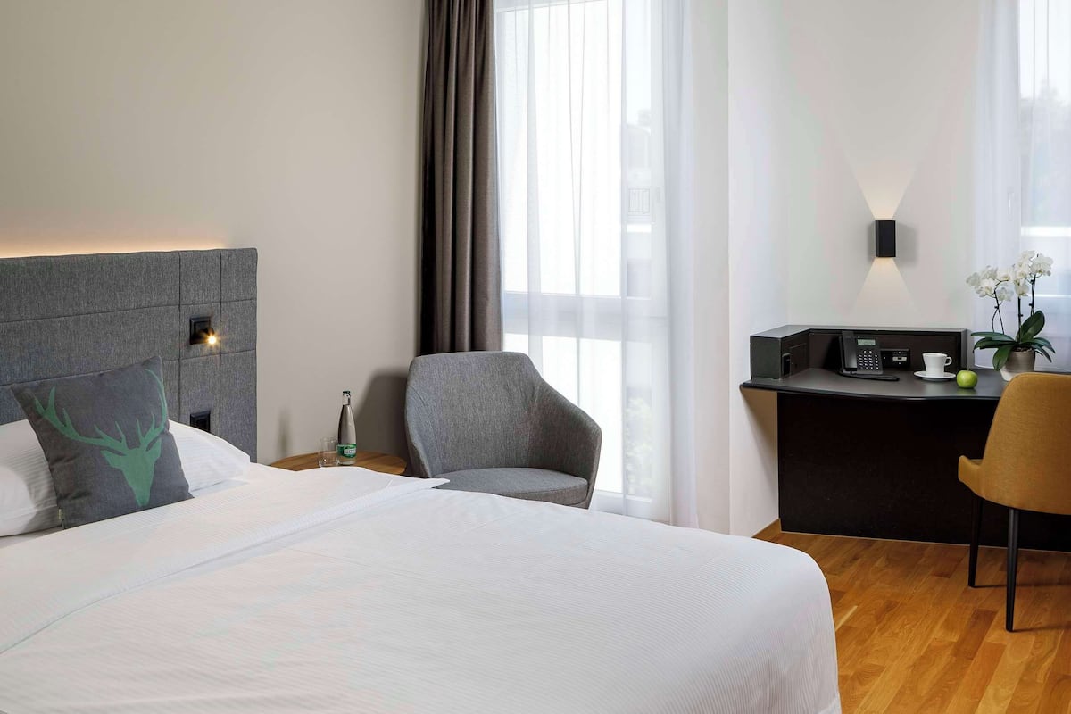 A modern hotel room with a large bed, a desk, and a chair.