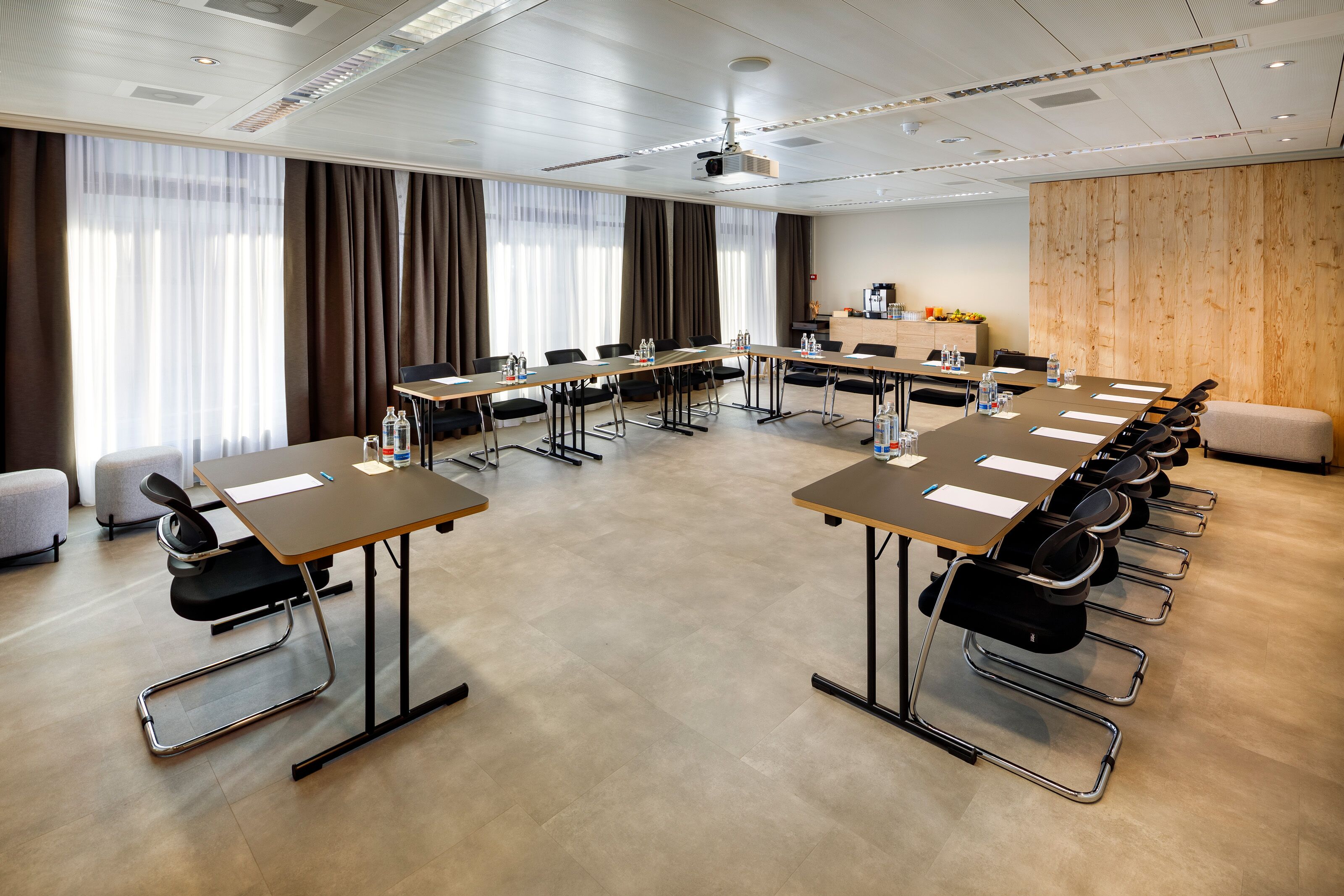 A conference room with multiple tables, chairs, a projector, and a wooden accent wall.