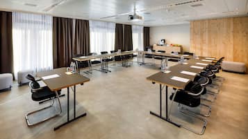 Un salón de conferencias con varias mesas, sillas, un proyector y una pared de madera decorativa.