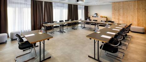 Un salón de conferencias con varias mesas, sillas, un proyector y una pared de madera decorativa.