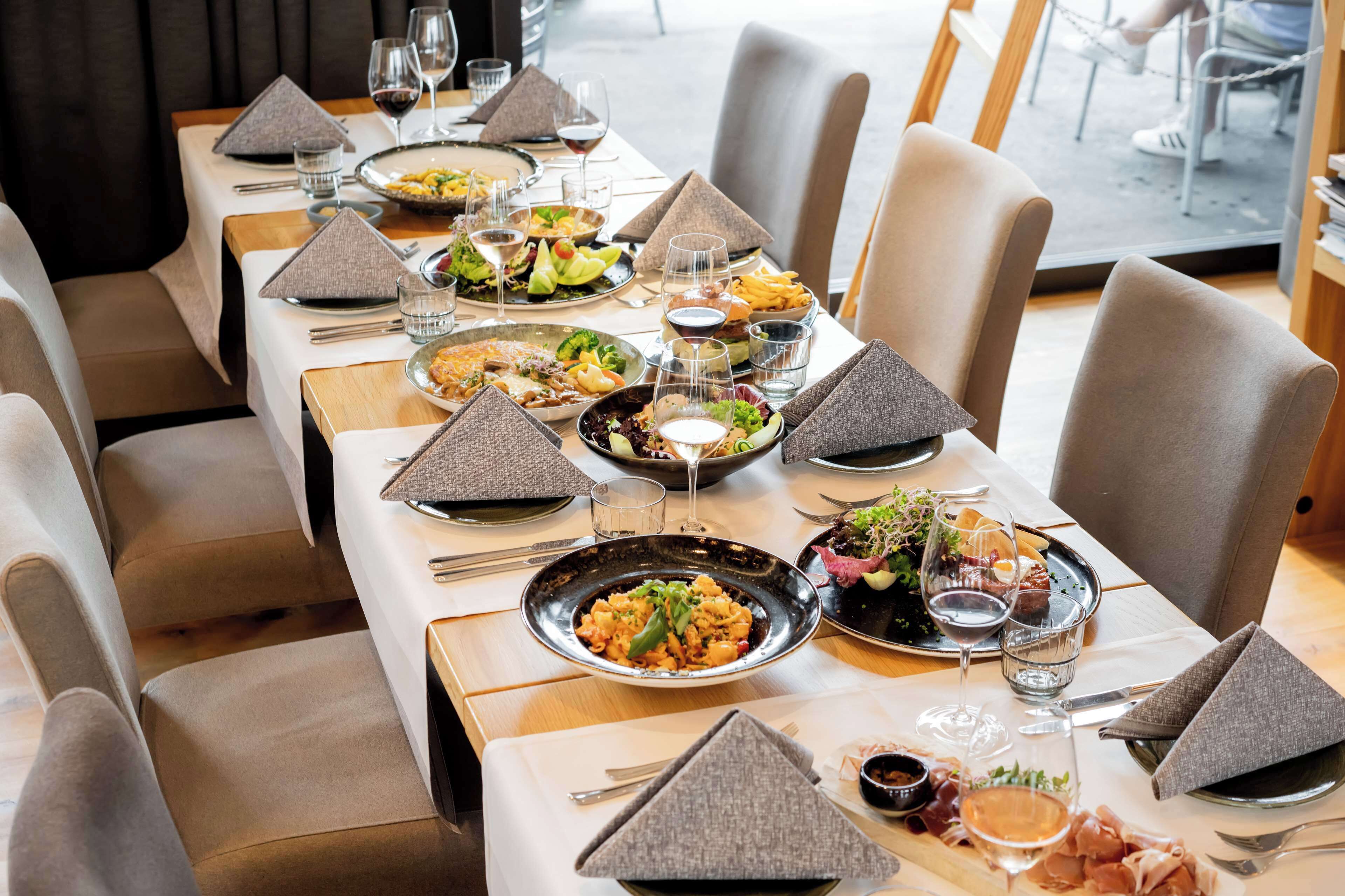 Un restaurante con varias mesas, cada una dispuesta con platos de comida, copas de vino y cubiertos ordenados.