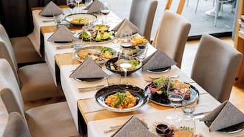 Un restaurante con varias mesas, cada una dispuesta con platos de comida, copas de vino y cubiertos ordenados.