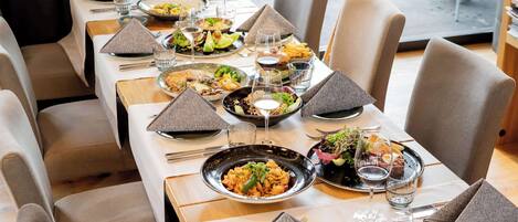 A restaurant setting with multiple tables, each set with plates of food, glasses of wine, and neatly arranged cutlery.