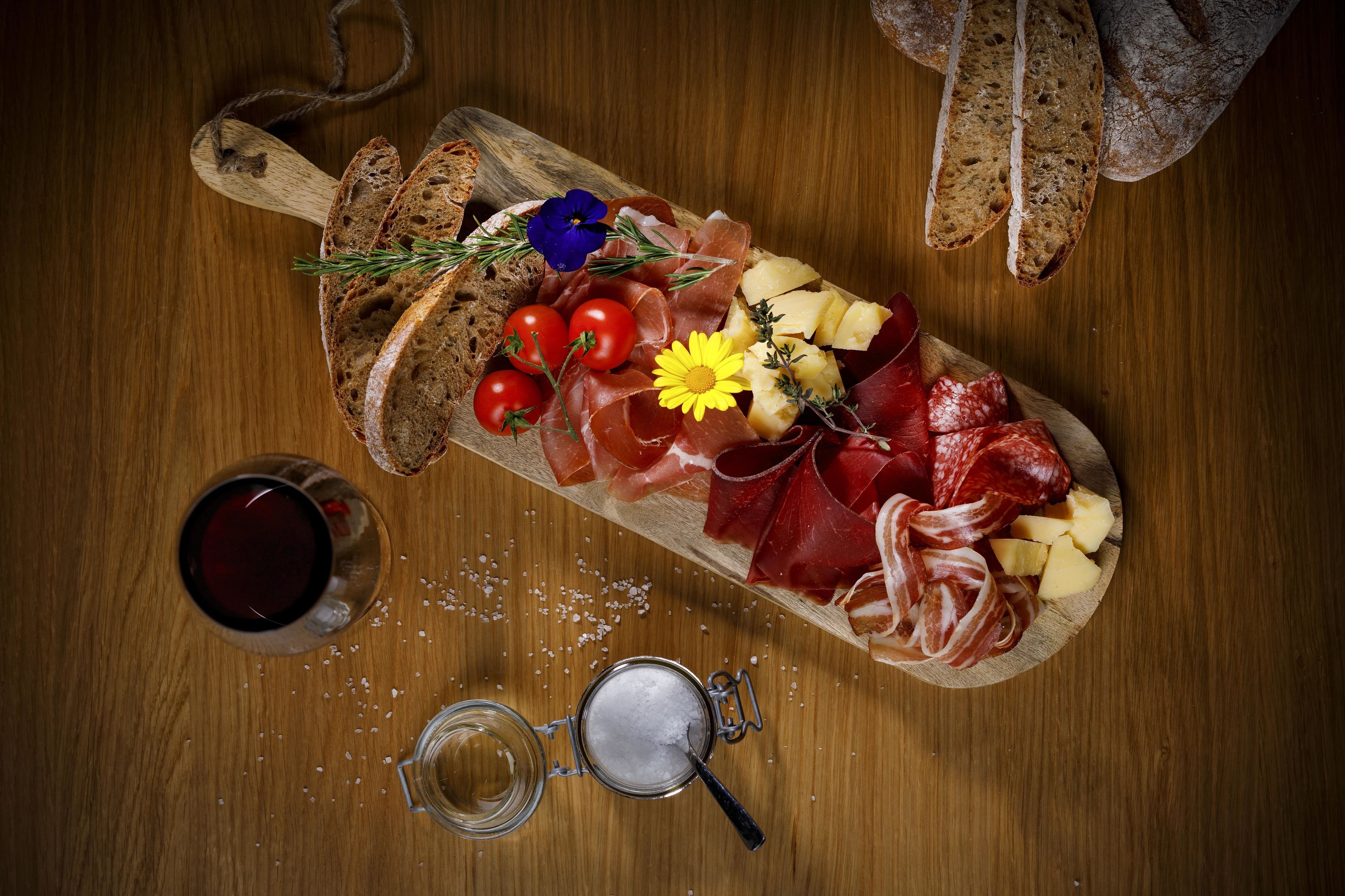 Una tabla de embutidos con diversos quesos, carnes y pan sobre una mesa de madera.