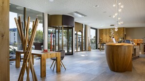 A modern interior with a wooden reception desk, a glass door entrance, and a view of the outside. - Hotel Allegra Lodge (Kloten)