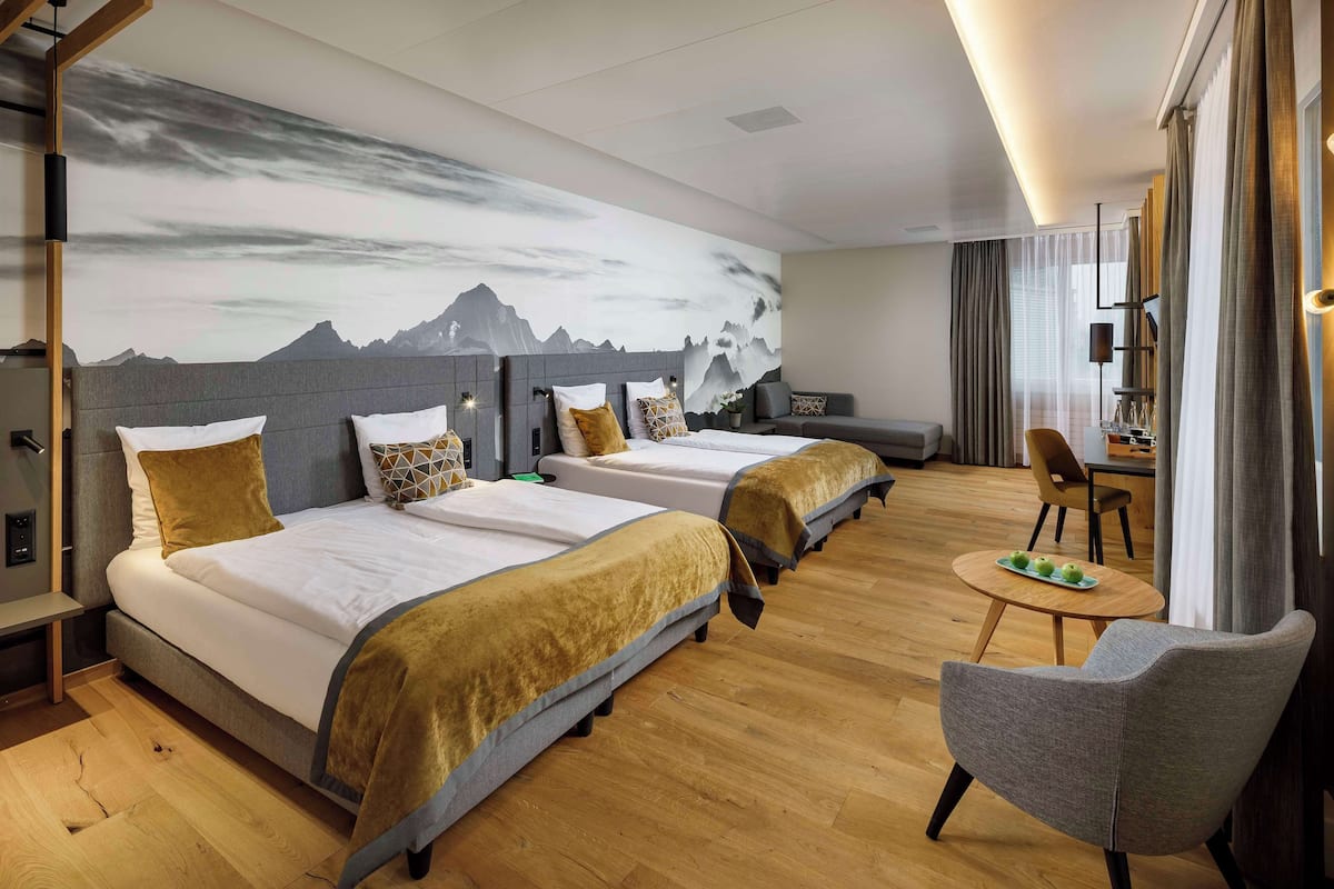 A hotel room with two beds, a sofa, a dining table with apples, and a chair.