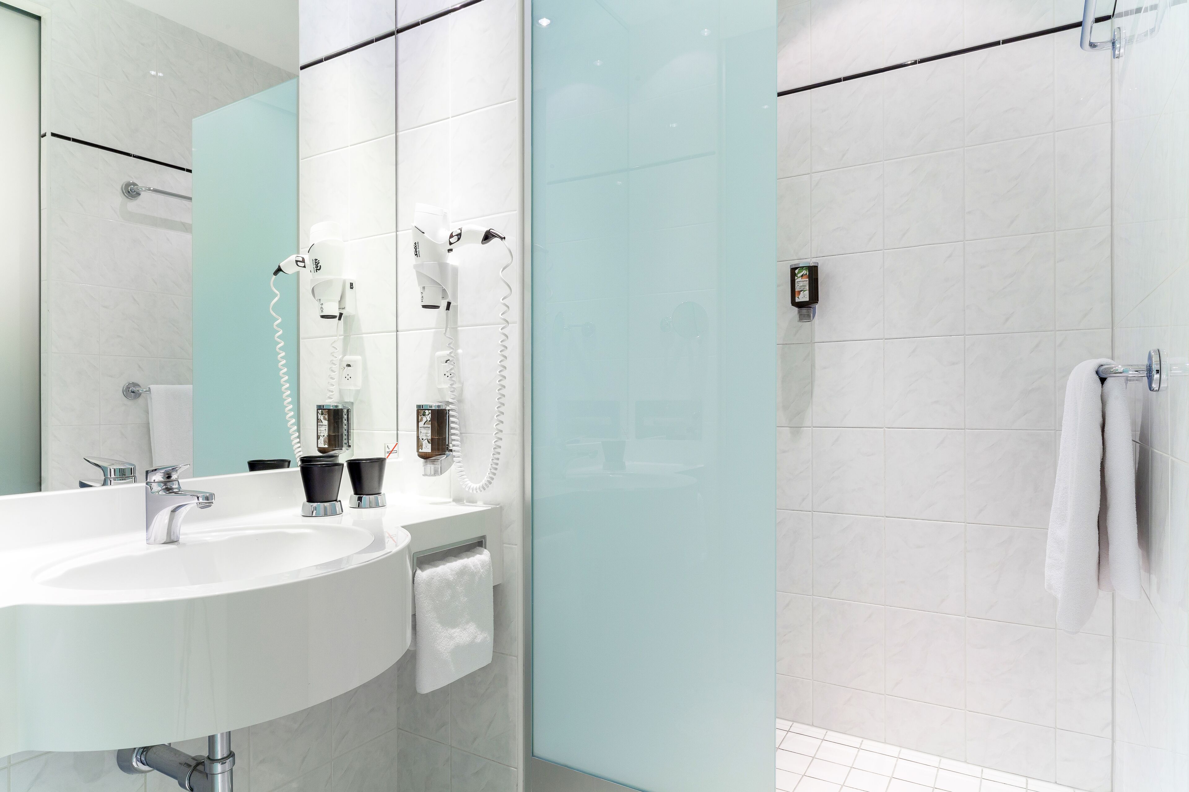 A modern bathroom with a white sink, a glass shower enclosure, and a towel rack.