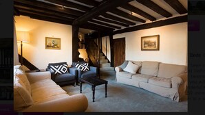 Ein gemütliches Wohnzimmer mit einer Couch, Sesseln und einem Couchtisch. Eine Treppe führt zu einer weiteren Ebene.
