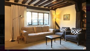 Ein gem ütliches Wohnzimmer mit einer Couch, einem Sessel und einem Couchtisch, ausgestattet mit sichtbaren Holzbalken und einem großen Fenster mit Vorhängen.