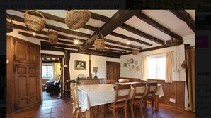 Ein rustikaler Essbereich mit Holztisch und -stühlen, einer hängenden Körbe und Blick auf ein gemütliches Wohnzimmer.