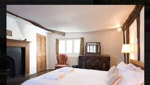 Ein Schlafzimmer mit einem großen Bett, einem Kamin, einem Holzschrank und einem Fenster mit Vorhängen.