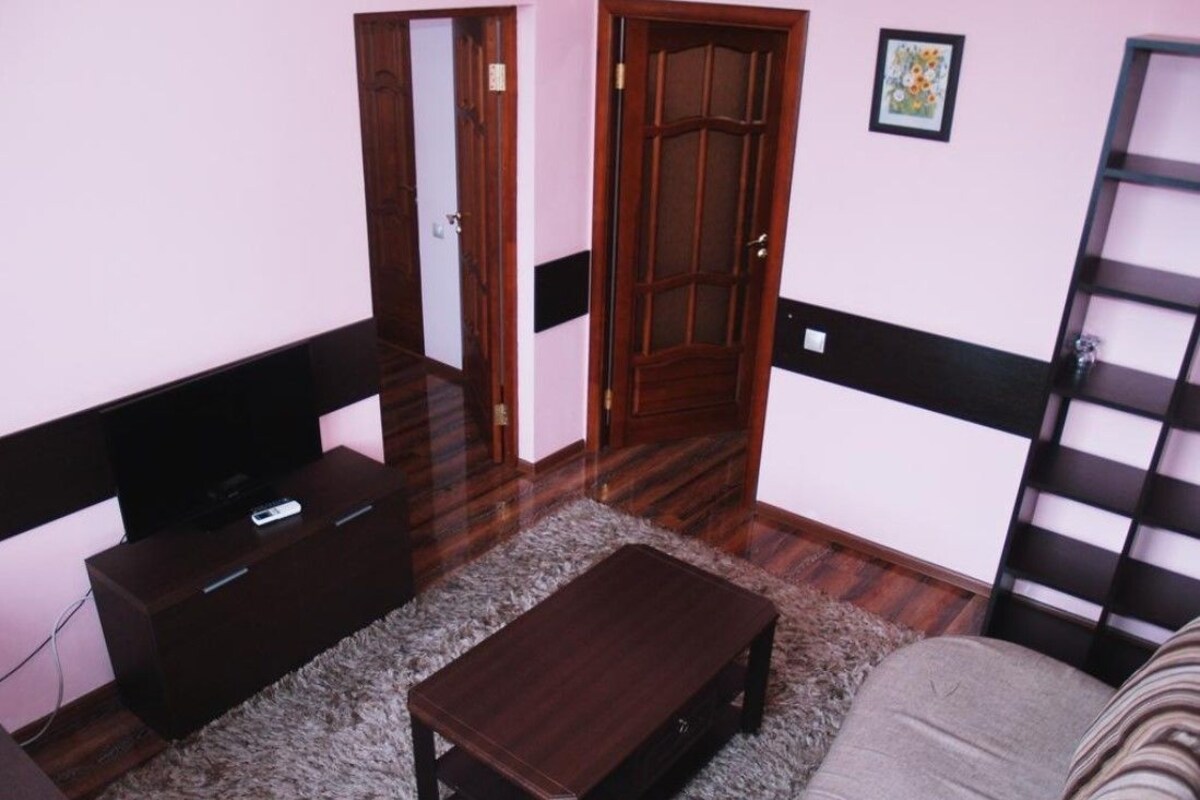 A living room with a dark wooden coffee table, a sofa, a TV on a stand, a door, and a bookshelf.