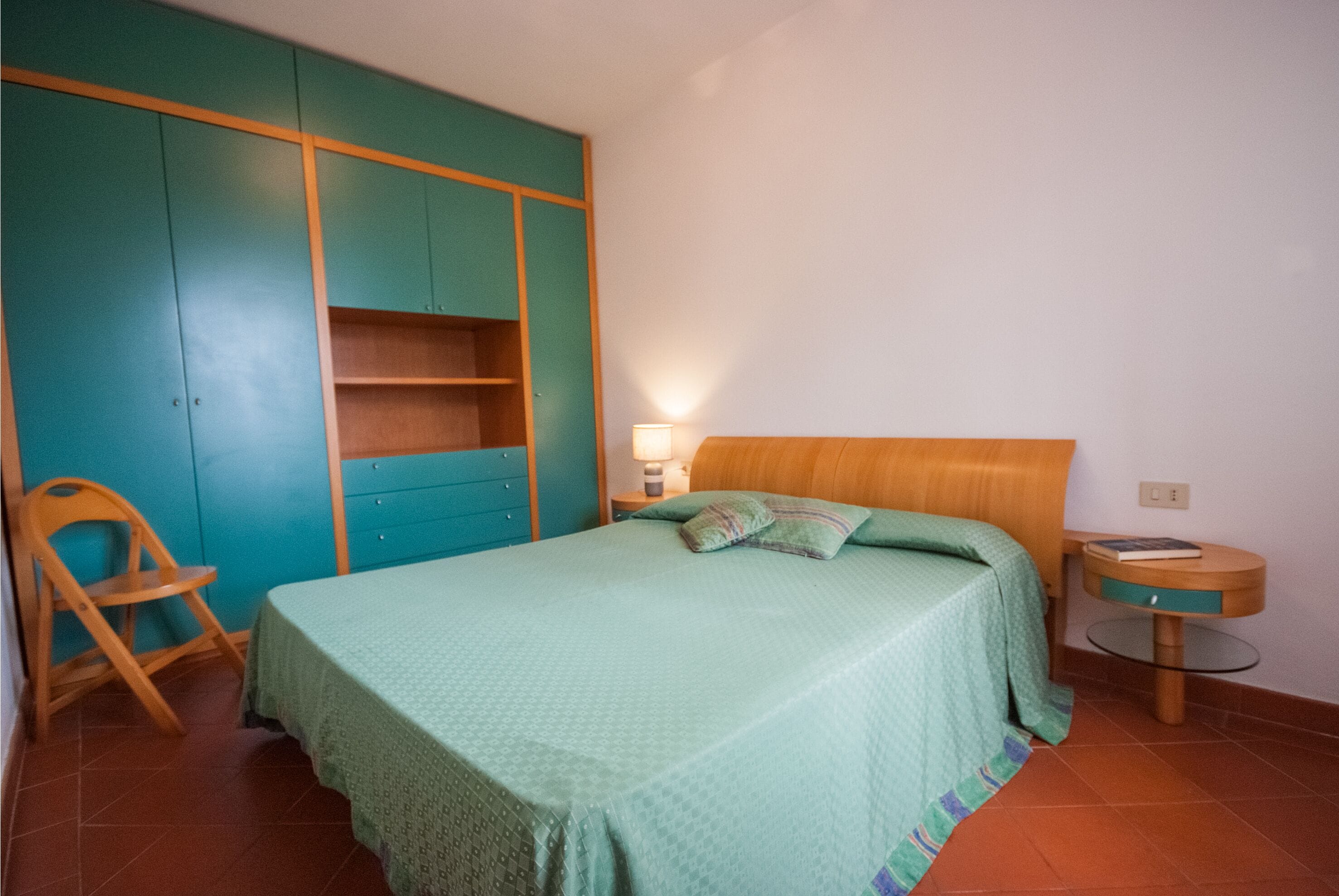 Ein Schlafzimmer mit einem Bett, einem hölzernen Kopfteil, einem Nachttisch, einem Sessel und einem Kleiderschrank.