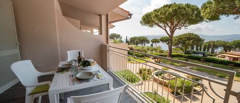 A balcony with a table set for dining, overlooking a landscaped garden and a body of water.