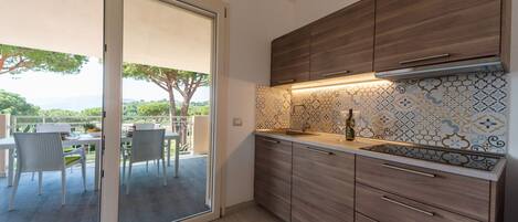 A modern kitchen with wooden cabinets, a tiled backsplash, and a sliding glass door leading to an outdoor dining area.