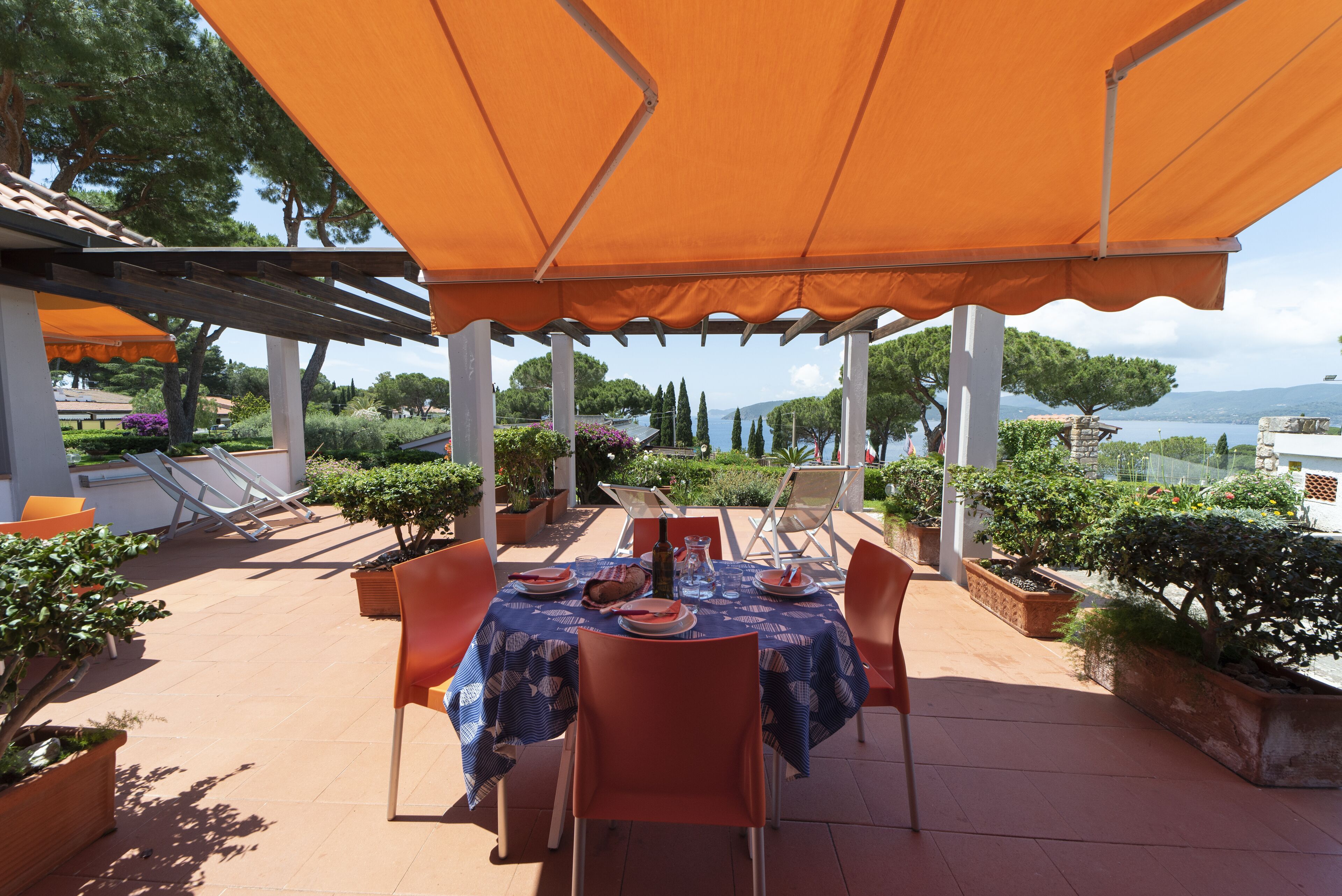 An outdoor patio with a table set for dining, surrounded by orange chairs and covered by a large orange canopy.