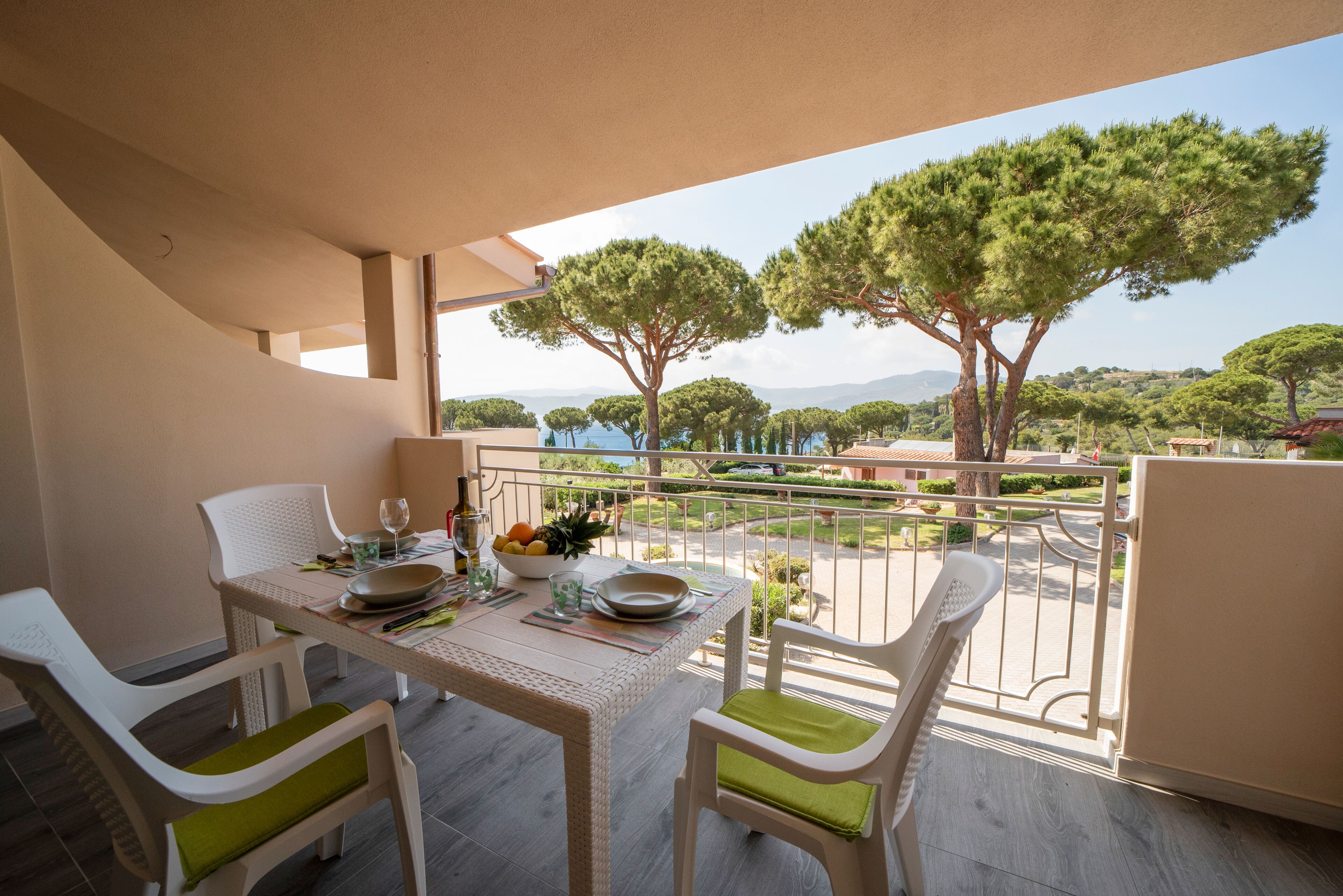 A balcony with a table set for two, chairs, and a view of trees and a body of water.