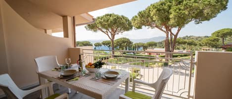A balcony with a table set for two, chairs, and a view of trees and a body of water.