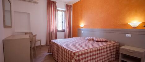 A bedroom with a checkered bedspread, a desk, a chair, a nightstand, and a wall-mounted lamp.