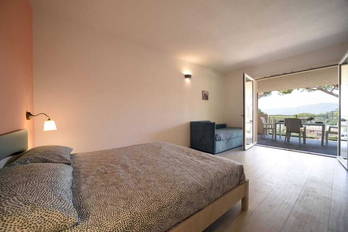 Une chambre à coucher comprenant un lit, une table de chevet, un bureau et une chaise. Il y a une fenêtre donnant sur l’extérieur.