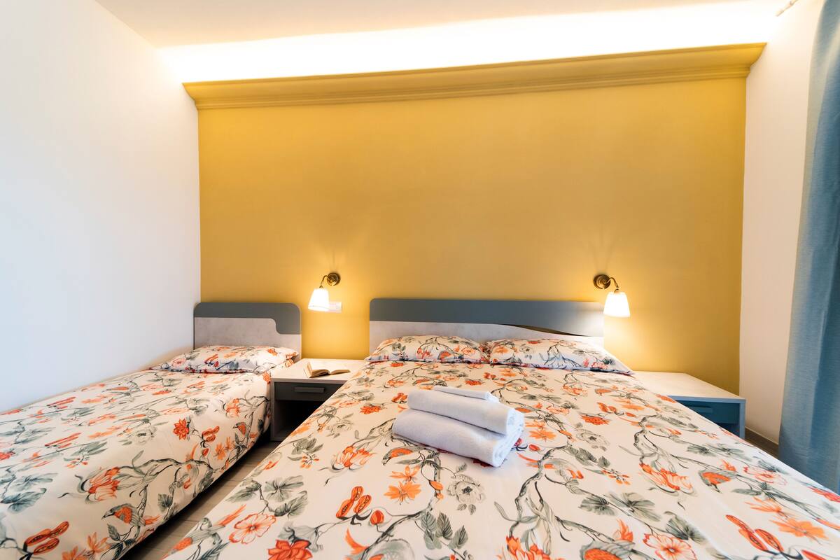 Une chambre d’hôtel avec deux lits simples, chacun agrémenté d’une literie à motifs floraux, d’une table de chevet et d’une lampe.
