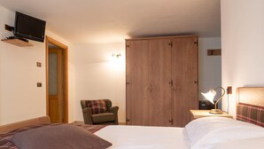 Un dormitorio con cama, una silla, armario, escritorio con lámpara y televisor montado en la pared.