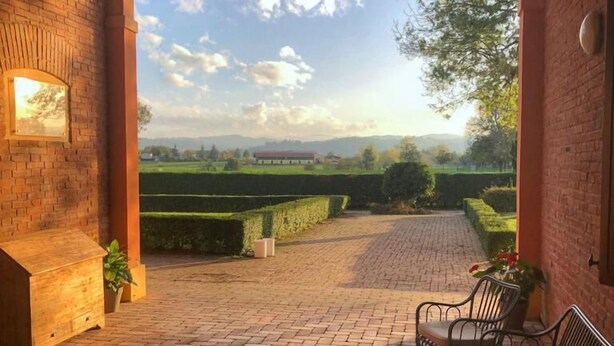 An outdoor patio with brick flooring, a wooden bench, and metal chairs. - Ca' Matilde (Quattro Castella)
