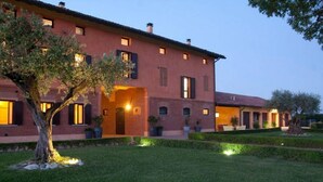 A large, two-story building with a brick facade, multiple windows, and a well-maintained lawn with trees. - Ca' Matilde (Quattro Castella)