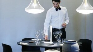 A dining area with a round table set for two, a waiter in a white shirt, and modern pendant lighting. - Ca' Matilde (Quattro Castella)