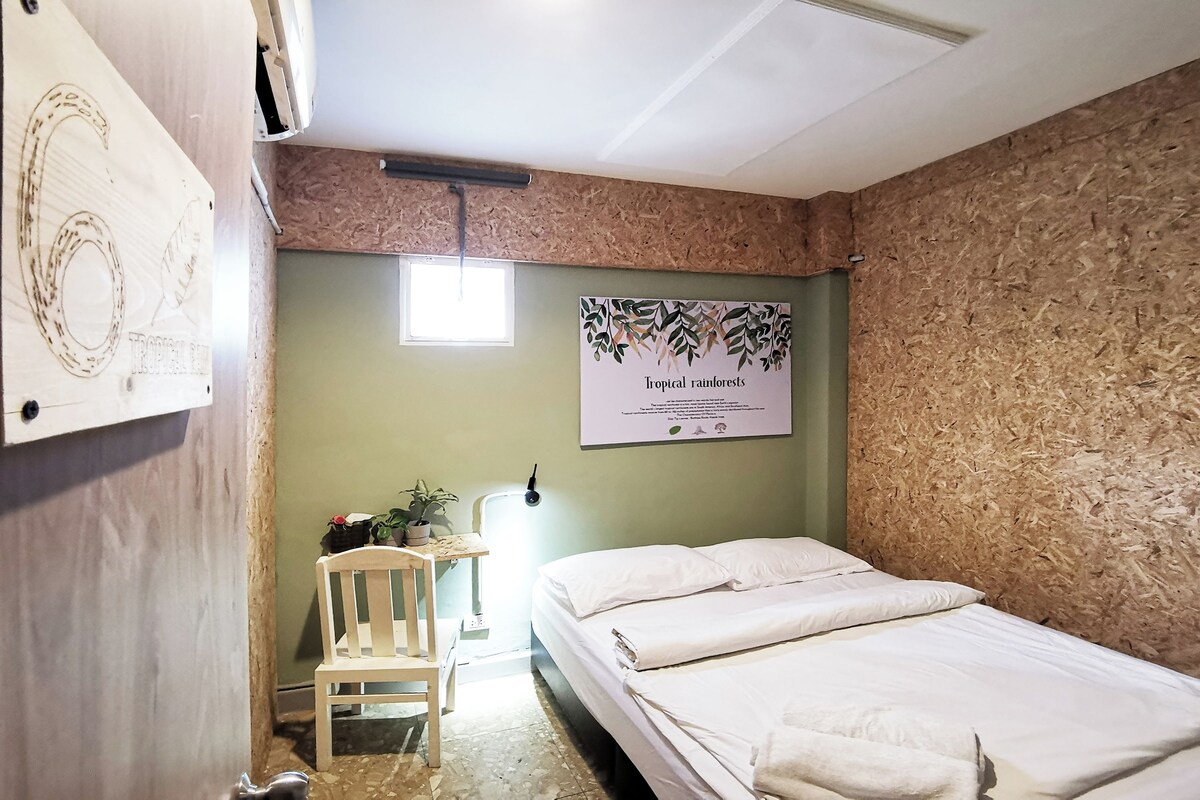 Una habitación con una cama, una mesita con una silla, un aire acondicionado instalado en la pared y una ventana.
