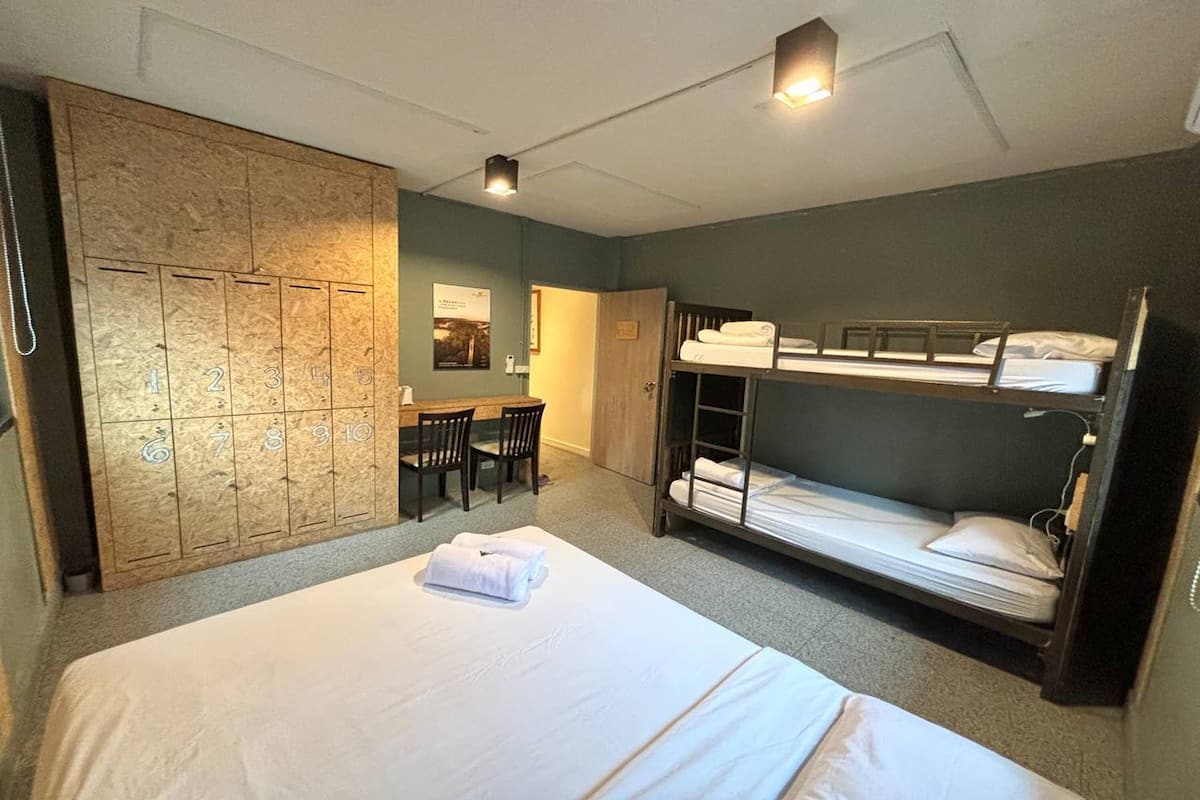Ein Hotelzimmer mit Etagenbetten, einem Schreibtisch, Stühlen und einem Schrank mit nummerierten Schließfächern.