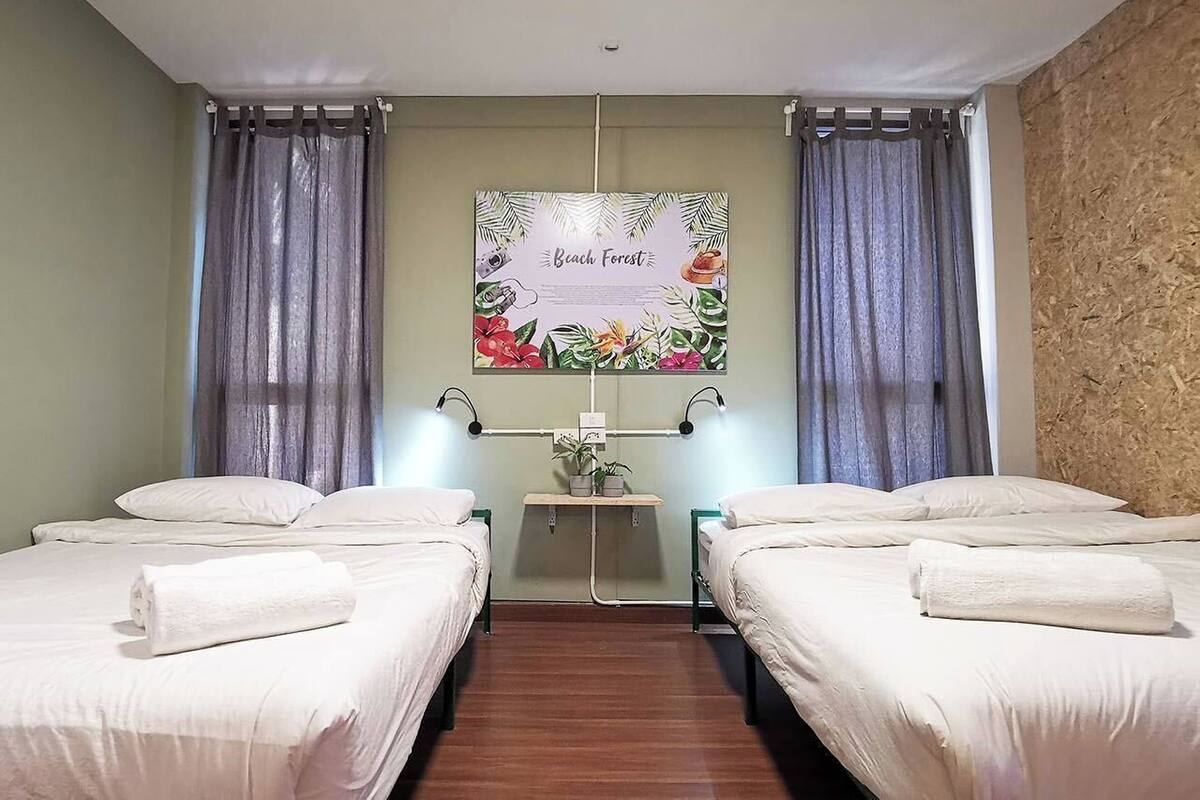 Ein Hotelzimmer mit zwei Betten, einem Wandbild mit dem Titel 'Beach Forest' und einem kleinen Tisch mit einer Lampe.