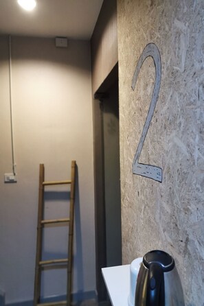 Una habitación con una escalera de madera apoyada en una pared, una pizarra blanca con el número '2' y una tetera sobre una mesa.