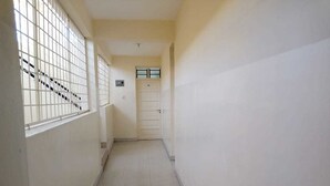 A narrow hallway with a tiled floor, a door at the end, and a window with bars on the left. - Metric Annex Hotel (Mombasa)