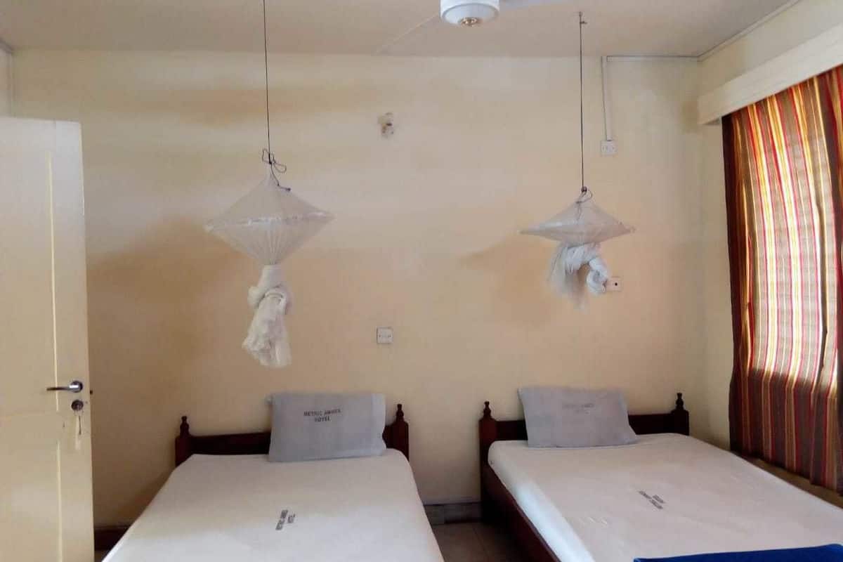 A hotel room with two beds, a ceiling fan, and a window with striped curtains.