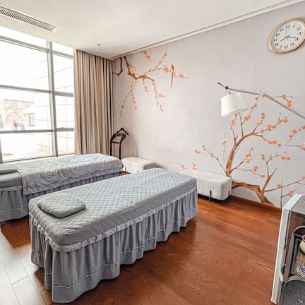 A hotel room with two beds, a large window, a wall clock, and a decorative tree mural.