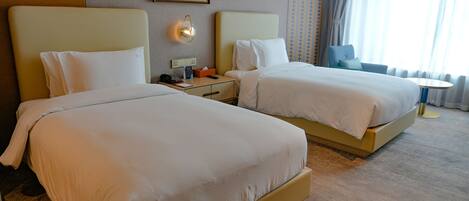A hotel room with two beds, a bedside table with a lamp, a small table, and a chair.