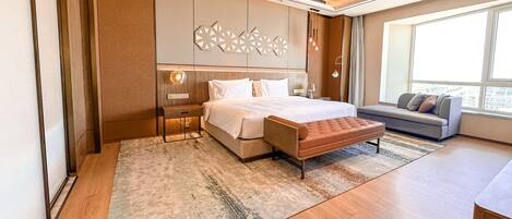 A modern hotel room with a large bed, a seating area, and a large window providing a city view.