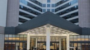 A modern building with a glass facade, a central entrance with a geometric light fixture, and a visible outdoor area with a fence. - Ethiopian Skylight Hotel (Addis Ababa)