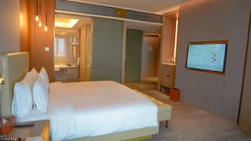 A hotel room with a bed, bedside table, lamp, and a TV mounted on the wall.